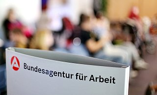 Ein Schild mit der Aufschrift „Bundesagentur für Arbeit“steht einem vollen Wartezimmer. Termine, die online vereinbart werden, sollen jetzt längere Wartezeiten vermeiden. - dpa