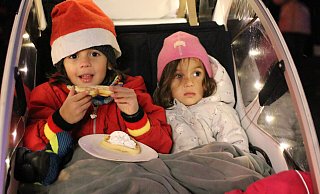 Ben Gieselmann (5) lässt sich die frische Waffel schmecken, während seine Schwester Sophie (3) die geschmückten Weihnachtsbäume und Hütten bestaunt. - Claus Frickemeier