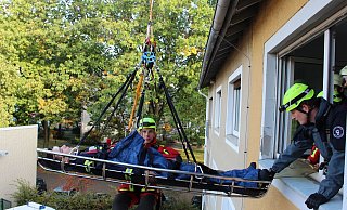 Maurice Vornholt in der Trage, Jannik Schröder (im roten Anzug hinter der Trage) und Christoph Wienstroer am Fenster proben den Ernstfall. - Stadt Gütersloh