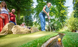 Zoe spielt den Golfball, beobachtet von Lena und Jan, in den Bachlauf, der den Ball in Richtung Loch trägt. Foto: Mike-Dennis Müller - Mike-Dennis Müller