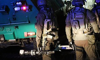 Polizisten des SEK stehen mit ihren Werkzeugen hinter einem gepanzerten Polizeifahrzeug in der Einfahrt zu einem Haus in Dortmund. In ganz NRW wurden mehrere Wohnungen durchsucht, sechs Rocker der Bandidos wurden verhaftet. - picture alliance/dpa
