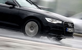 Ein Auto fährt durch eine riesige Pfütze. Fährt es zu schnell oder sind die Reifen nicht im besten Zustand, kommt es dann schnell zu Aquaplaning. - Verwendung weltweit
