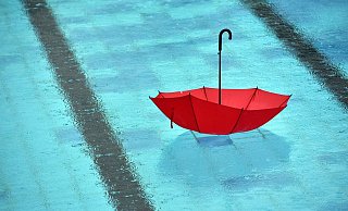 Ein Symbol für den verregneten Sommer in OWLs Freibädern: Ein roter Regenschirm treibt in einem leeren Schwimmbecken. - Ralf Hirschberger/dpa-Zentralbil