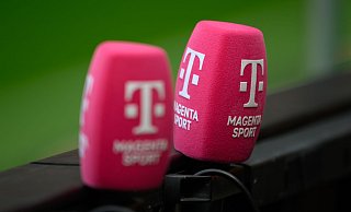 Zwei Mikrofone von Magenta Sport stecken an einer Bande bei einem Fußballplatz. - Robert Michael/dpa
