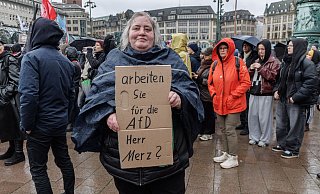 Eine Demonstrantin in Hamburg stellt auf einem Pappschild eine Frage an Bundeskanzler Friedrich Merz (CDU). - Markus Scholz/dpa