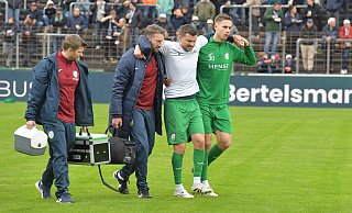Ein ganz bitterer Moment: Noch vor dem Anpfiff des Derbys gegen den SC Wiedenbrück wird Björn Rother (m.), Kapitän des Fußball-Regionalligisten FC Gütersloh, unter anderem von Mitspieler Jannik Borgmann (r.) vom Platz begleitet. Der 29-Jährige hat sich zuvor beim Warmmachen schwer verletzt. - Jens Dünhölter