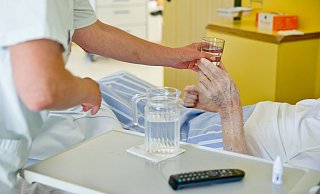 Eine Krankenpflegerin reicht einem Patienten ein Glas Wasser. - Daniel Karmann/dpa