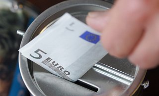 Ein Fünf-Euro-Schein wird in eine Spendendose gesteckt. Die Weihnachtszeit ist eine Zeit des Gebens. - picture alliance / Bernd Thissen/dpa