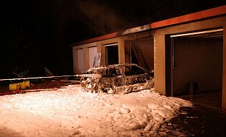 Das ausgebrannte Autowrack wurde von den Einsatzkräften mit einem Gurt aus der Garage gezogen. Der Löschschaum bedeckte großflächig den Hof. - Polizei Kreis Minden-Lübbecke