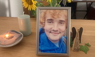 Ein letztes Foto von Max (Name von der Redaktion geändert) steht zusammen mit einer Kerze, einem Schutzengel und leuchtend gelben Sonnenblumen auf dem Esstisch der Familie. - Ivonne Michel