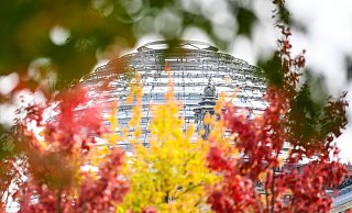 Rot-gelb-grün herbstlich verfärbte Blätter sind an Bäumen vor der Reichstagskuppel zu sehen. - Foto: Britta Pedersen/dpa-Zentralbild/dpa