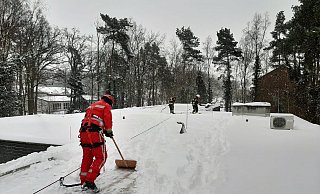 Mit Schneeschiebern und Besen machte man der kalt-weißen Pracht auf dem langen Flachdach des Gebäudes den Garaus und beförderte sie herunter. - Feuerwehr Espelkamp