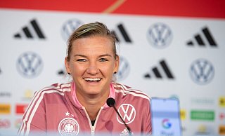 Die deutsche Kapitänin Alexandra sitzt während einer Pressekonferenz lachend auf dem Podium. - Michael Memmler/Eibner-Pressefoto/dpa