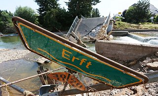 Ein Hinweisschild auf die Erft liegt in Stolzenheim vor einer zerstörte Brücke im Schutt. Der Einsatz im Rheinland und in Rheinald-Pfalz wird die künftige Ausrüstung der heimischen Wehren beeinflussen. - David Young/DPA