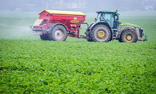 Ein Traktor fährt mit einem Streuwagen über ein Feld und bringt Dünger aus. - dpa
