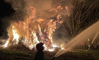 Als es auf der Lohe stockdunkel ist, entzünden die Besucher ein mächtiges Osterfeuer. Damit die Flammen nicht auf die umliegenden Bäume übergreifen, halten Brandbekämpfer Wasserpistolen auf die Äste. - Elke Niedringhaus-Haasper