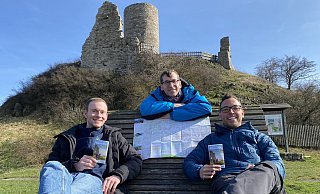 Touristiker Lucas Lambracht (v. l.), Bürgermeister Tobias Scherf und der Mobilitätsbeauftragte Jan Kolditz präsentieren am Desenberg die neue Wanderkarte. - Stadt