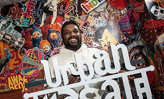 Thanujan Sivanathan präsentiert sein neues Restaurantschild vor bunter indischer Fototapeten-Kulisse. - Jörg Dieckmann - www.dieckmann-fotodesign.de