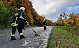 Mit Besen und Bindemittel rücken freiwillige Feuerwehrkräfte auf der Bundesstraße 239 an der Abtei Marenmünster der Ölspur zuleibe. - Madita Schellenberg