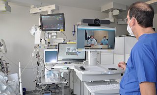 Chefarzt Torsten Meier steht auf der Intensivstation vor dem Televisitenwagen: Auf dem Bildschirm sind Moritz Lersch und Tom Unger von der Intensivstation des Uniklinikums Münster zu sehen. Gemeinsam entscheiden die Spezialisten über die Behandlung der Patientin. - Brüderkrankenhaus