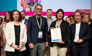 Bundesministerin Steffi Lemke (r.) und VZBV-Vorständin Ramona Pop (l.) zeichnen das Goerdeler-Gymnasium aus. Die Lehrkräfte Silke Michels und Sebastian Niggemann (Mitte) nehmen in Berlin als Mitglieder der Steuergruppe Urkunde und Schulplakette entgegen. - VZBV/Fabian Sommer