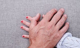 Eine Männerhand liegt auf einer Kinderhand. (gestellte Szene). - Annette Riedl