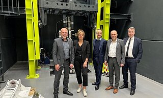 Am Teststand für Luftfahrtfahrwerke bei der Heggemann AG versammeln sich (v. l.) Robert Heggemann (Inhaber und Aufsichtsratschef), NRW-Wirtschaftsministerin Mona Neubaur, Stefan Berndes (Bundesverbandes der deutschen Luft- und Raumfahrtindustrie), Landrat und Fughafen-Aufsichtsratschef Christoph Rüther und Harald Cremer (Aerospace NRW). - Heggemann AG