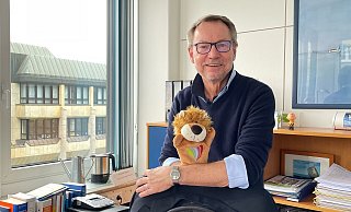 Andreas Spilker an seinem Schreibtisch, den er zum Monatsende räumt. Auf der Hand hat der Sam, den Löwen. Das ist das Maskottchen, das vom Jugendamt entwickelt wurde, um Kinder gegen sexualisierte Gewalt zu stärken. Sam steht für stark, achtsam, mutig - und Sam sagt nein. Für Spilker ist der Kinderschutz immer das zentralste Element der Arbeit im Jugendamt gewesen. - Natalie Gottwald