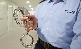Ein Polizeibeamter zeigt auf dem Archivbild Handschellen. - Oliver Krato