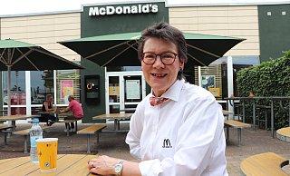 Mit einem Pfefferminztee und einem Wasser sitzt Gabriele Conert, ein gesticktes M und den Schriftzug "Ich liebe es" auf der Brusttasche, vor ihrem McDonald's. - Marion Pokorra-Brockschmidt