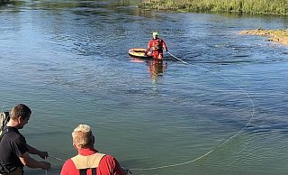 Ein angeleinter Feuerwehrmann im Überlebensabzug sichert das angetriebene Kanu. - Feuerwehr Paderborn