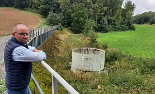 Ortsvorsteher Hubertus Kuhaupt weist auf Einlauf, Damm und Spundwand des Rückhaltebeckens hin. Die Dimensionen des Bauwerks sind strittig. - Dieter Scholz