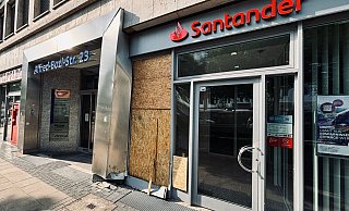 Am Tag nach dem Unfall ist die beschädigte Schaufensterscheibe der Sanstander-Filiale bereits mit Brettern gesichert. Der Eingangsbereich aus Metall ist sichtlich verbogen. - Eike J. Horstmann