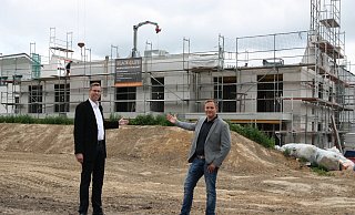 Die Geschäftsführer Matthias Bohnhorst (links) und Marcel Gehrmann stehen auf dem noch zu bebauenden Gelände und weisen auf die bereits dahinter entstehenden Mehrfamilienhäuser ihrer Projektgesellschaft Place4Life. - Britta Bohnenkamp-Schmidt