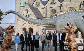 Die Organisatoren von "Dinoborn" posieren vor dem Paderborner Dom mit dem an einem Baum naschenden Diplodocus. - Maria Kalemi