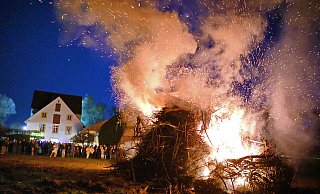 Funken sprühen in die Nacht, als das Osterfeuer an der Wassermühle zu Bentrup so richtig in Fahrt kommt - drumherum stehen und sitzen Menschen, die den lauen Abend genießen. - Barbara Franke