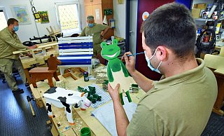 Kevin (im Vordergrund), Jörg (hinten links) und ein weiterer Gefangener der JVA Bielefeld-Brackwede fertigen Holzfiguren. Die werden dann bei knastladen.de verkauft. Der grüne Frosch im Vordergrund bekommt noch einen Schirm. - Barbara Franke