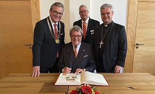 Reinhard Zinkann, geschäftsführender Gesellschafter der Miele & Cie. KG in Gütersloh, unterzeichnet im Beisein von (v. l.) Bürgermeister Michael Dreier, Gildemeister Johannes Beverungen und Erzbischof Udo Markus Bentz im Goldenen Buch der Stadt Paderborn. - Stadt Paderborn