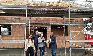 Bürgermeister Lars Bökenkröger (r.) und Valeria Usatschov von der Wirtschaftsförderung (l.) übergeben ein Geschenk zur Einweihung des Rohbaus an die Hausherren Karine Pfeifer und Benedikt Mertens. - Elke Niedringhaus-Haasper