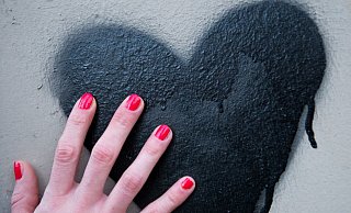 Eine Frauenhand mit rot lackierten Fingernägeln berührt in Berlin ein schwarzes Herz, das auf eine Mauer gesprüht wurde. - Verwendung weltweit