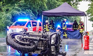 Die schwarze Yamaha liegt auf der Brockhagener Straße. Im Hintergrund schirmen Rettungskräfte den Blick auf den Patienten ab. - Paul Brinkmann