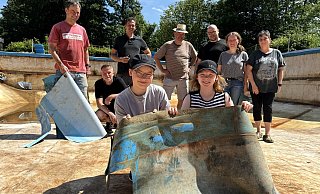 Andreas Kassing (hinten v.l.), Michael Koch, Florian Skeide, Bernd Kröger, Lars und Tatjana Brinkmann, Meike Plaß-Wittland und (vorn v.l.) Mona und Sarah Brinkmann zeigen Stücke der zerschnittenen Folie. Insgesamt haben mehr als 20 Helferinnen und Helfer im Lenzibad geholfen. - Andreas Sundermeier