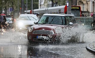 Ein Auto fährt während eines Gewitters im Regen durch eine Pfütze. - Oliver Berg/dpa