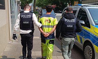 In Handschellen wird ein Mitarbeiter zum Zivilfahrzeug der Polizei gebracht, damit sie auf der Dienststelle die Personalien des Mannes feststellen kann. - Claus Frickemeier