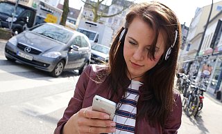 Eine junge Frau hört Musik, während sie eine Nachricht auf dem Handy schreibt. Das ist nicht verboten, aber im Straßenverkehr sehr gefährlich. - Symbolfoto: picture alliance / dpa