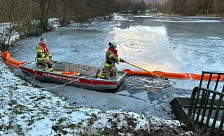 Aus dem Boot heraus bringen Einsatzkräft der Warburger Feuerwehr eine Ölsperre am Überlauf des Korintenteichs in Hardehausen an. - FFW Warburg