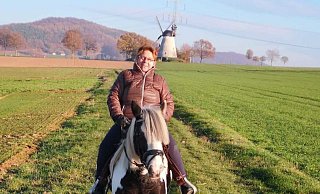 Brunhild Homann bei einem Ausritt auf ihrem Pferd. Die Holländerwindmühle Struckhof im Hintergrund ist namensgebend für den Schnathorster Ortsteil. - Brunhild Homann