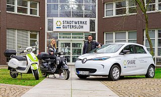 Die beiden Mobilitätsmanager Lara Wölm und George Gabriel mit E-Roller und E-Auto, die zur Flotte des E-Carsharings der Stadtwerke Gütersloh gehören. - Stadtwerke Gütersloh