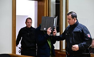 Der Angeklagte wird in den Gerichtssaal des Landgerichts Oldenburg geführt. Ihm wird vorgeworfen, im Juni 2023 in Vechta nach der Trennung von seiner Lebensgefährtin, einer gebürtigen Rhda-Wieeenbrückerin, diese heimtückisch mit einem Messer ermordet zu haben.Sina Schuldt/dpa - Sina Schuldt/dpa