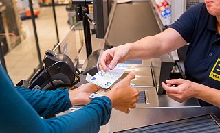 Eine Frau lässt sich an einer Kasse in einem Supermarkt Bargeld auszahlen (gestellte Szene). Foto: Benjamin Nolte - picture alliance / dpa Themendienst